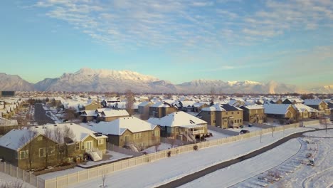 Panorámica-Aérea-Lenta-Sobre-Un-Barrio-Pintoresco-En-Un-Día-Despejado-Después-De-Una-Tormenta-De-Nieve-Con-Montañas-Al-Fondo