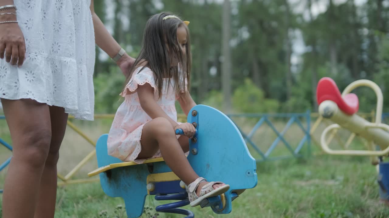 una madre embarazada y su hija joven disfrutan de un tiempo de juego juntos en un patio de recreo en el parque, rodeados de árboles y vegetación