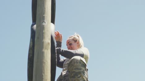 mujer soldado caucásica sonriente bajando la pared de neumáticos en la carrera de obstáculos del ejército en el sol