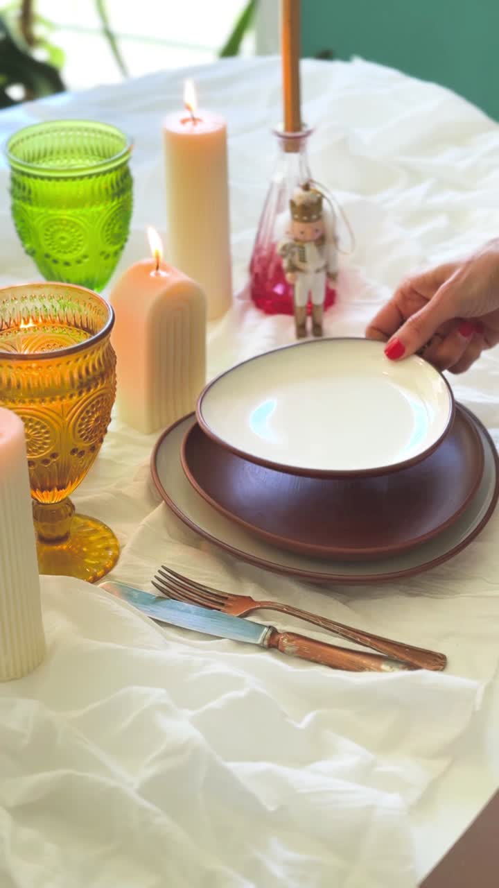 Mano che apparecchia un'elegante tavola da pranzo con piatti e candele accese
