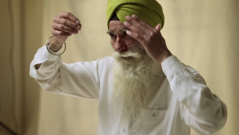 Fotografía-De-Estudio-De-Un-Hombre-Sikh-Mayor-Con-Barba-Que-Se-Coloca-Una-Aguja-De-Salai-En-Un-Turbante-Contra-Un-Fondo-Liso,-Filmado-En-Tiempo-Real