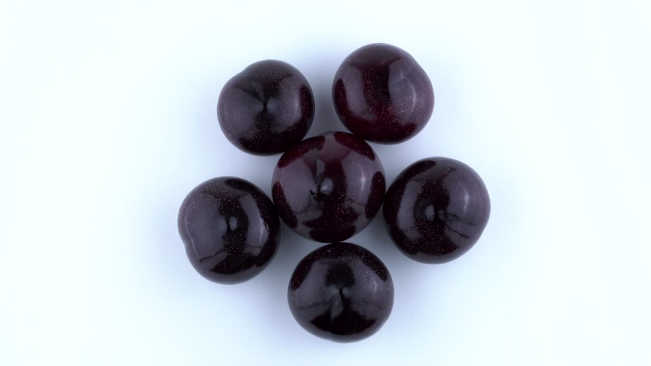 Top view from above of a few big purple plums. Rotating on the turntable. Isolated on the white background. Closeup. Macro.