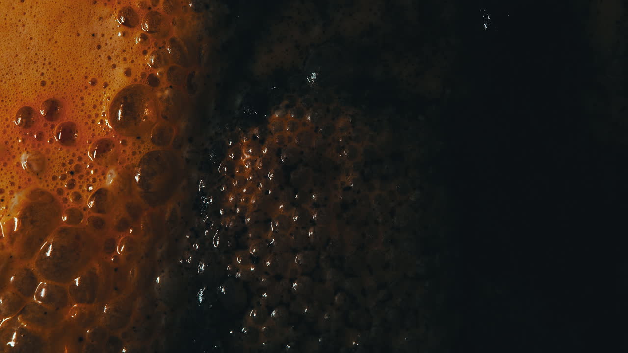 Liquido di colore arancio-nero che sale e ribolle. Primo piano.