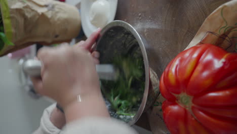 close-up of hands mixing fresh herbs in a metal bowl to make pesto