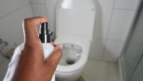 a hand holding a toilet spray bottle in front of a toilet