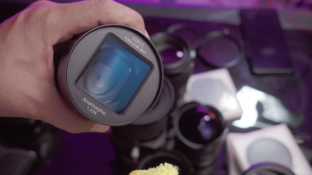 Person holding and cleaning a camera lens in a studio setup with multiple lenses on display