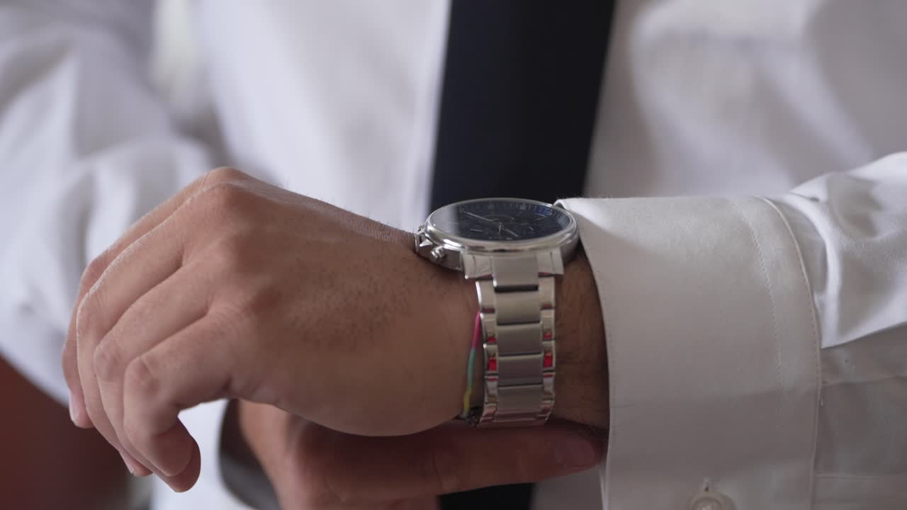 Close up of a man in a white shirt and black tie adjusting a silver watch