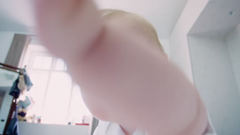 baby boy sitting on parents bed reaching out towards camera