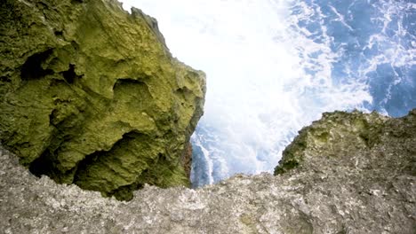 pov adventurer looks over mossy green seacliff to see jagged rock and strong wave