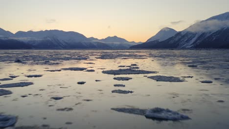 Flying-low-over-cold-water-with-ice-sheets-in-Cook-Inlet-during-sundown,-aerial