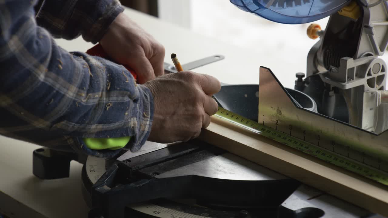 A man measures a baseboard and cuts it using his table saw.