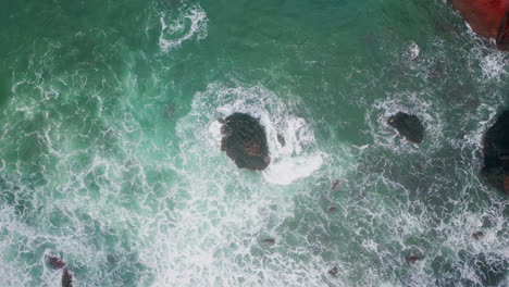 Top turquoise sea splashing rocks. Drone view of powerful ocean water washing