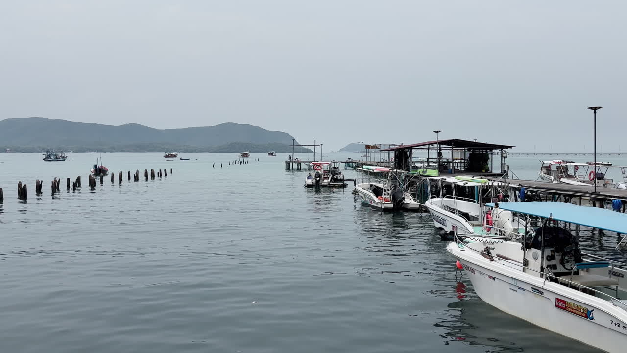 Inquadratura fissa di un tranquillo porto di pescatori a Samae San vicino a Pattaya, Thailandia, con piccole imbarcazioni ormeggiate vicino a un molo vuoto. Mare calmo, senza persone, atmosfera pacifica che suggerisce bassa stagione, destinazione di viaggio.