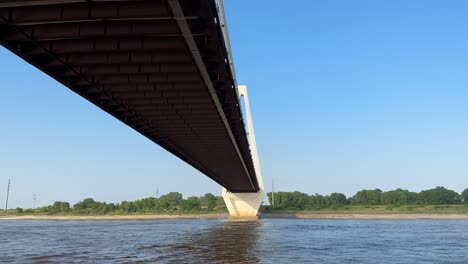 Punto-De-Vista-En-Primera-Persona-Viajando-En-El-Agua-Bajo-El-Puente-Conmemorativo-De-Los-Veteranos-De-Stan-Musial-En-St-Louis-Missouri-En-Un-Día-Soleado