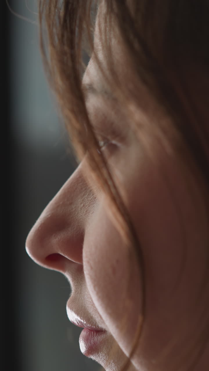 Young woman looks into light window intently sitting in room. Sad woman waits for return of family watching street. Face of tranquil lady closeup