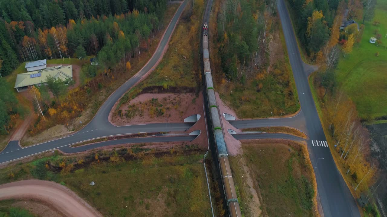 Aerial, tilt, drone shot, tracking and following a long cargo train, driving in a forest, towards a town, on a cloudy fall day, in Uusimaa, Finland