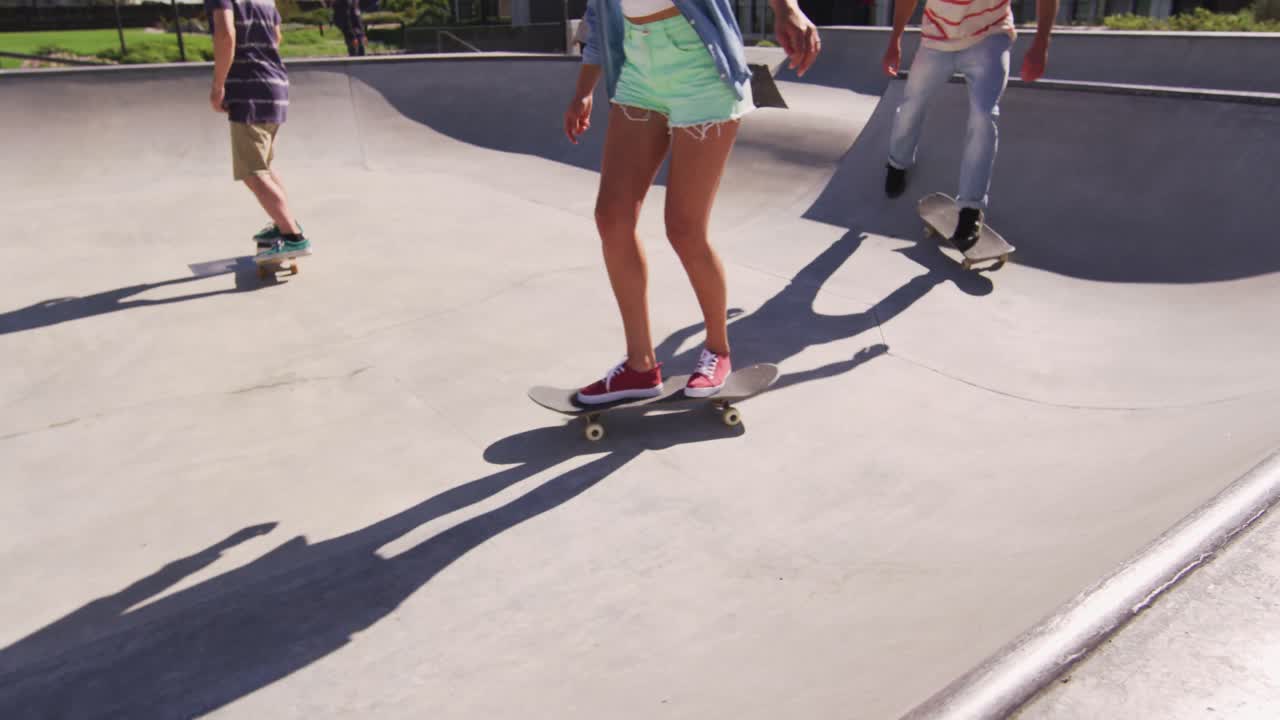 Low section of caucasian woman and two male friends skateboarding on sunny day