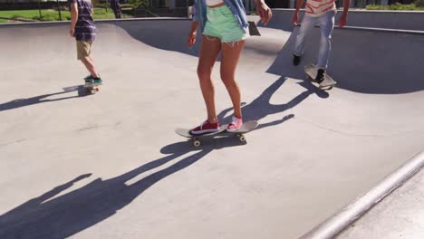 Low-section-of-caucasian-woman-and-two-male-friends-skateboarding-on-sunny-day