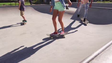 sección baja de la mujer caucásica y dos amigos masculinos patinaje en un día soleado