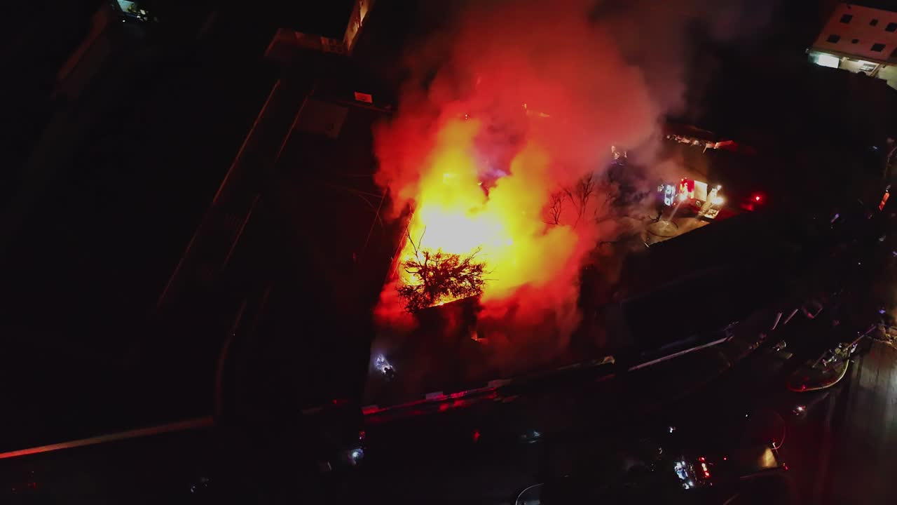 Warehouse on fire at night, with fire trucks and police cars responding to the emergency incident, Dominican Republic. Aerial drone orbiting