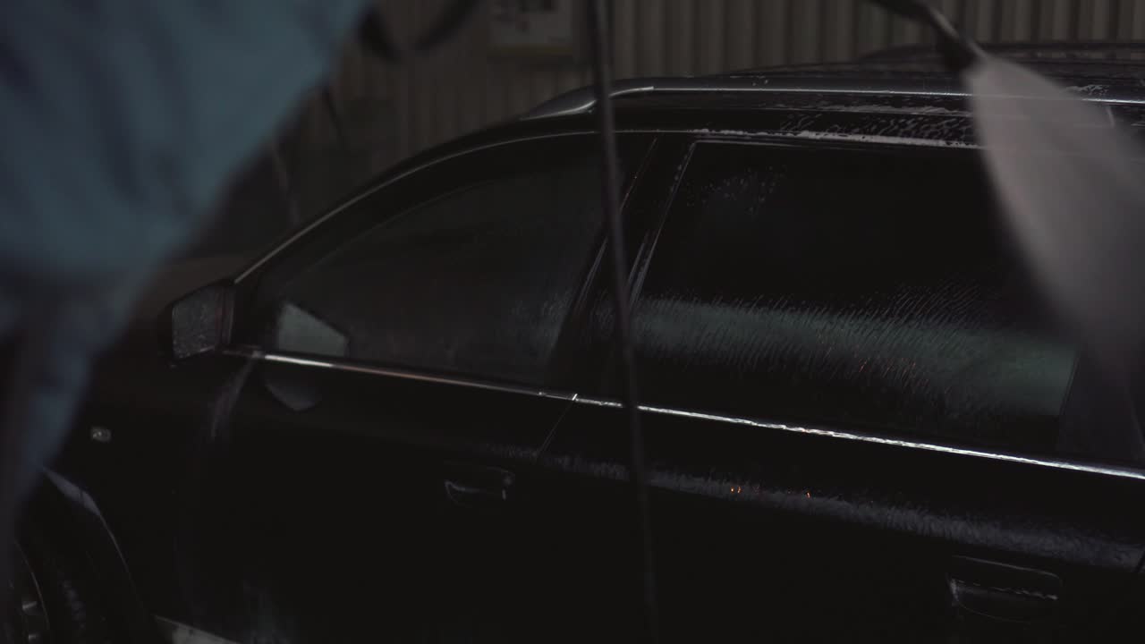 Hand holding water pressure cleaner and washing car or applying wax,side view