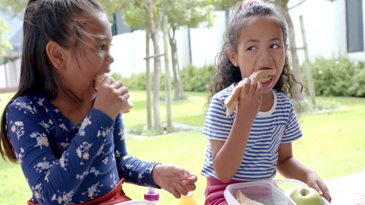 In school, two biracial young girls enjoying lunch outdoors