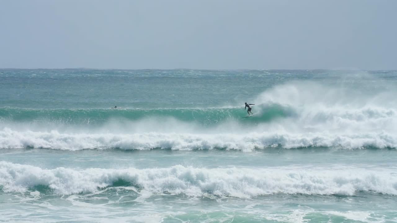 un surfista cayendo en una ola en aguas cristalinas, con el viento de la costa en cámara lenta