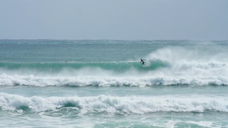 Un-Surfista-Cayendo-Sobre-Una-Ola-En-Aguas-Cristalinas,-Con-Viento-Marino-En-Cámara-Lenta