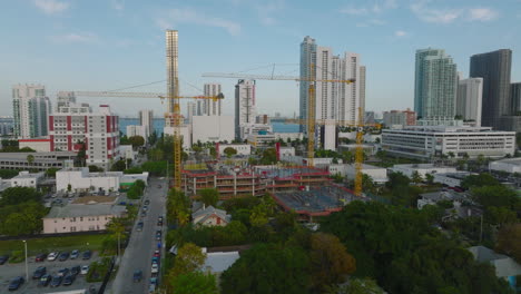 Slide-and-pan-shot-of-group-of-tower-cranes-on-construction-site-of-new-modern-high-rise-building.-Miami,-USA