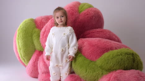 young girl in white knitted outfit with large pink and green fluffy pillows