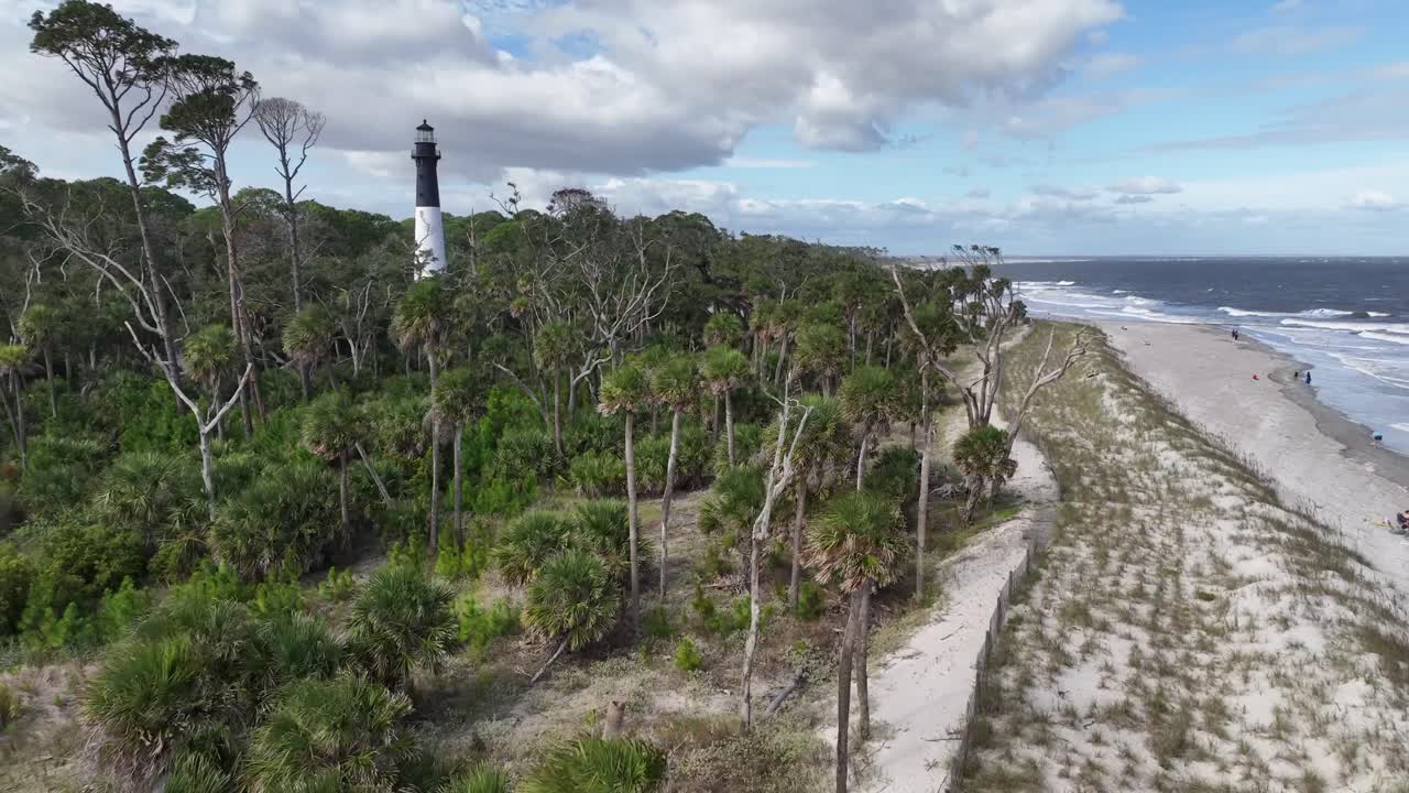 aerial rising past palmetto trees toward the huntiing island beach lighthouse in south carolina