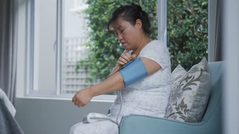 집 에서 소파 에 앉아 혈압 측정기 를 사용하는 아시아 여성