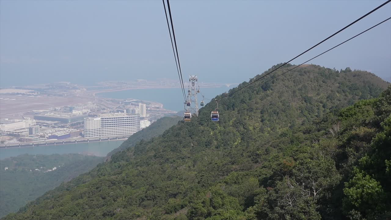 Vista aerea della funivia Ngong Ping 360 che scende su montagne lussureggianti con lo sfondo dell'Aeroporto Internazionale di Hong Kong