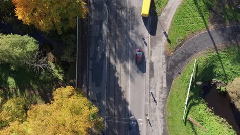 aerial of quiet road in autumn with moving car and shadows of tall golden trees