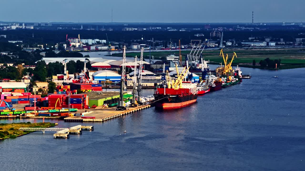 Wide aerial of container ships docked at a bustling seaport lined with colorful cargo containers and cranes over calm blue waters