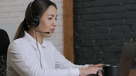 smiling woman call centre operator, customer support agent wears headset consults client online typing on laptop, talk in internet computer chat, helpline operator secretary make conference video call