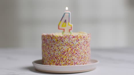 studio shot birthday cake covered with decorations and lit candle celebrating fourth birthday being blown out