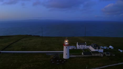 aerial orbit around the illuminated loop head lighthouse, revealing the atlantic ocean at dawn