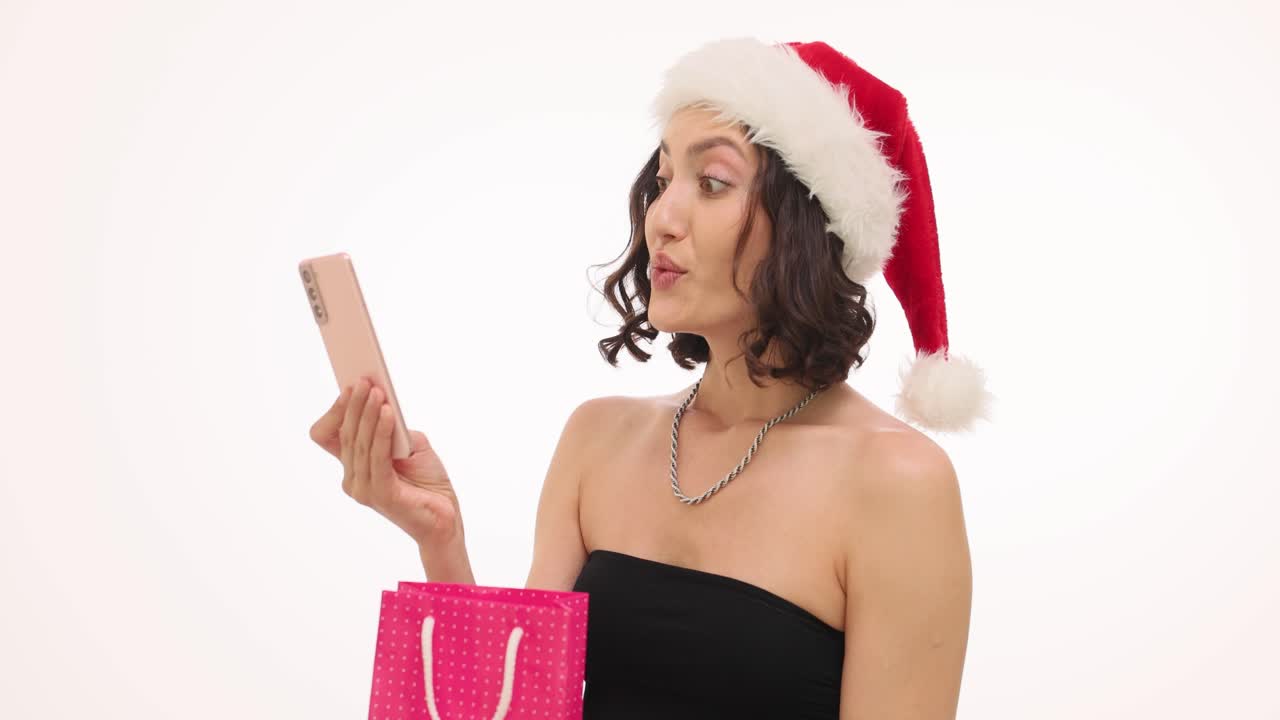Woman with Santa hat looking surprised at a gift in a shopping bag