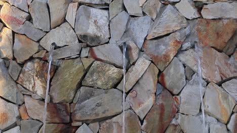 three spouts through rock wall creates simple urban water fountain