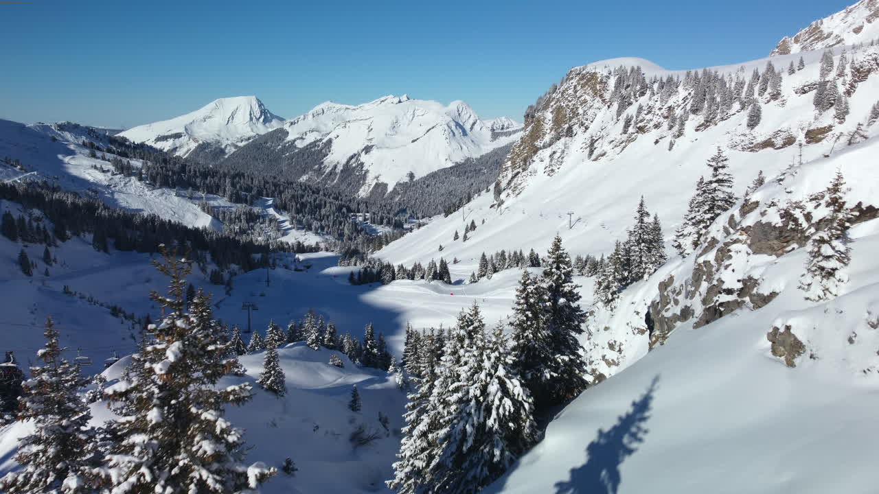 Tiefer Überflug durch das Hinterland des Skigebiets Avoriaz in den französischen Alpen in Richtung einer präparierten Skipiste.