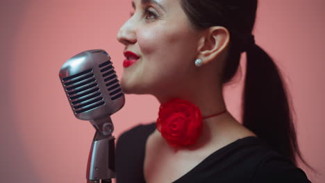 primer plano de una cantante apasionada con labios rojos, con una cinta roja en el cuello, cantando en un micrófono vintage, mientras la cámara se aleja lentamente