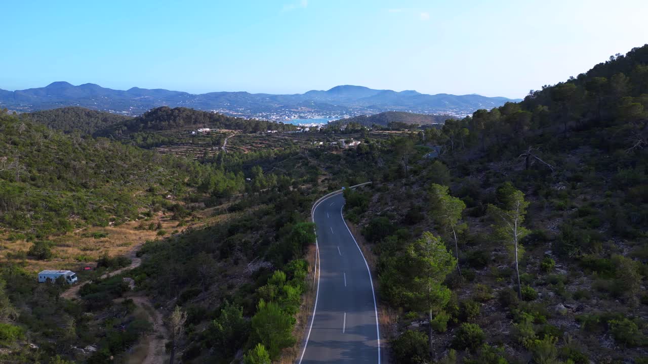 empty Road winding through a vibrant green forest in Ibiza, Spain, leading down towards the beautiful San Antonio Bay. Stunning aerial view flight panorama overview drone
