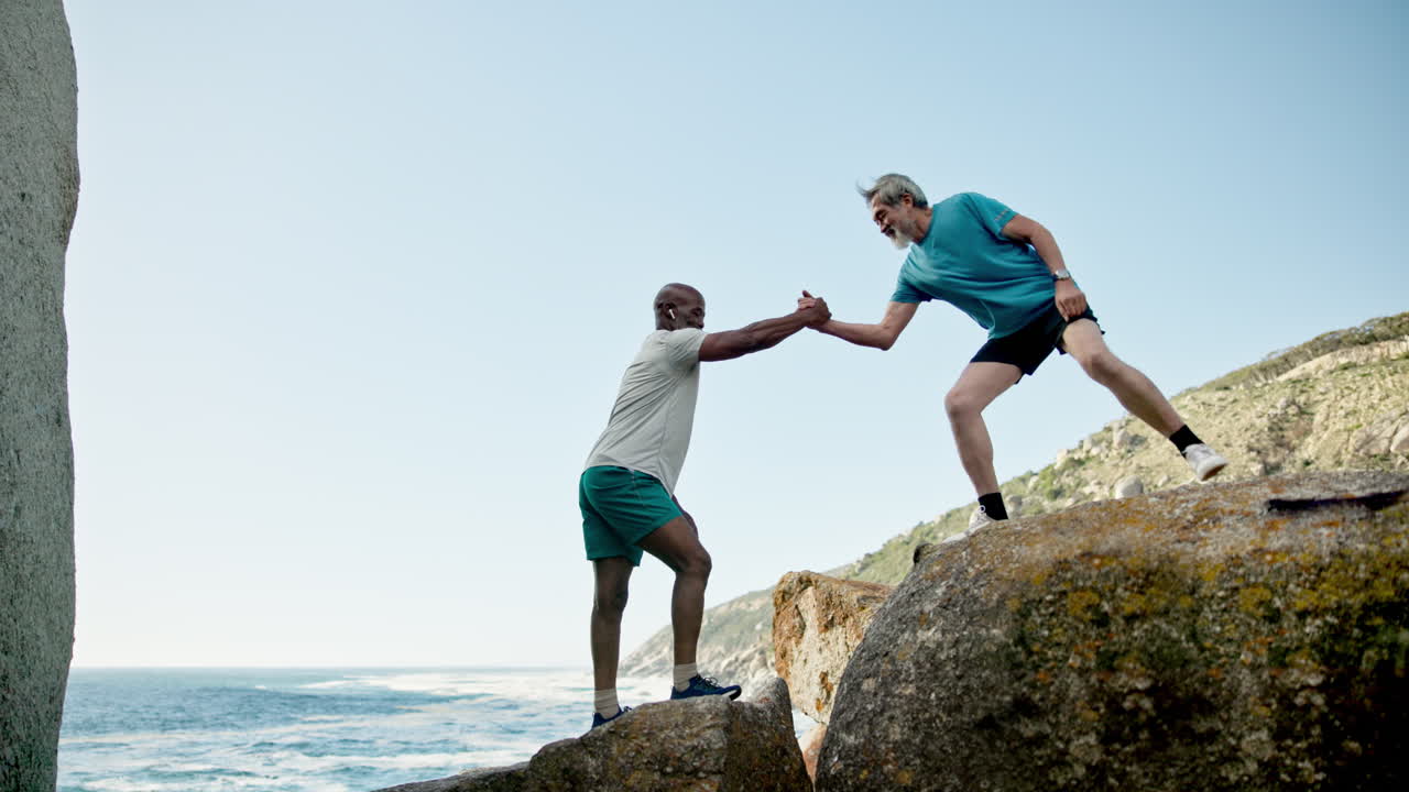 Two men helping each other rock climbing outdoors by the ocean