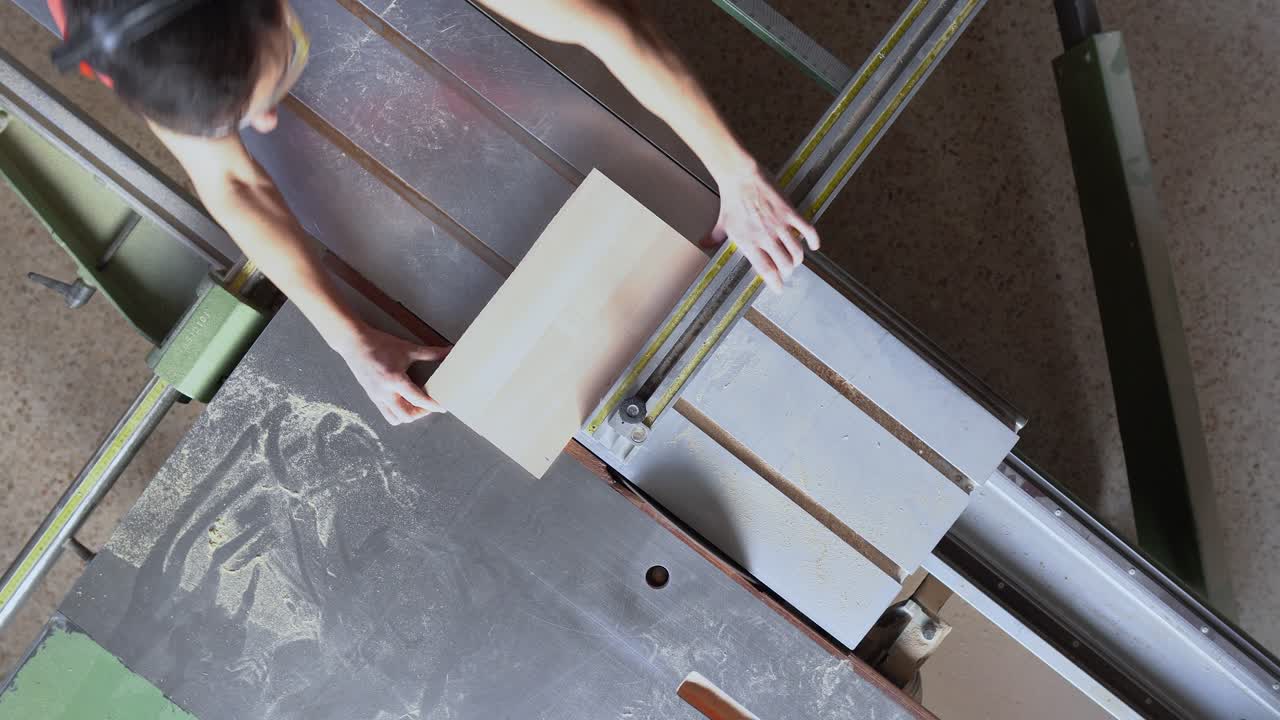 Overhead view of a woodworker cutting timber on a panel saw in a workshop