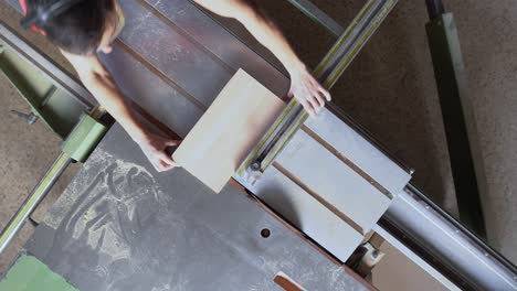 overhead view of a woodworker cutting timber on a panel saw in a workshop