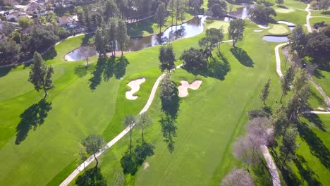 4k drone shot of country club golf course in los angeles, california on a warm, sunny day with ponds and lush fairways with white sand bunkers