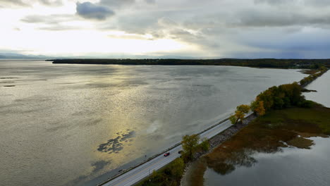 Huge waterscape of the lake is crossed by the highway. Cars ride by the road. Overcast sky above the panorama. Aerial view.