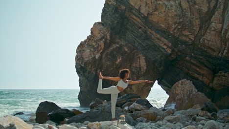 woman practicing pose dancer on rocky seacoast. girl training balance on nature.