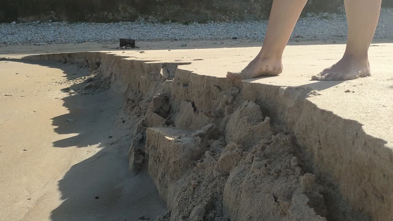 Barefoot person steps on sand cliff edge, sand collapses at Torimbia beach Asturias
